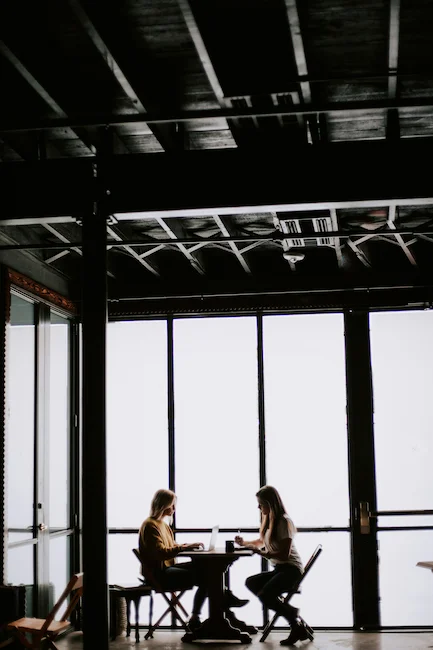 Deux femmes travaillant ensemble une stratégie digitale sur leurs ordinateurs dans un espace de coworking moderne avec une grande baie vitrée