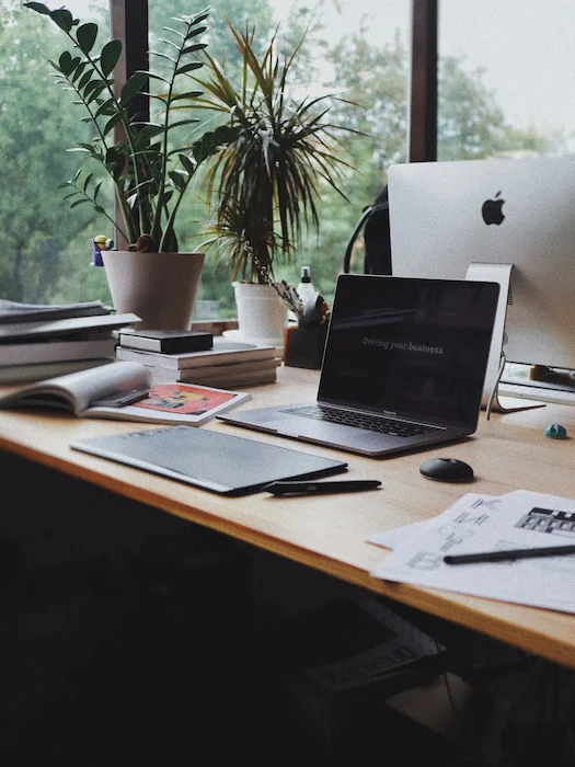 Bureau de travail moderne avec ordinateur portable, iMac, plantes vertes et cahiers, environnement inspirant pour le travail à distance