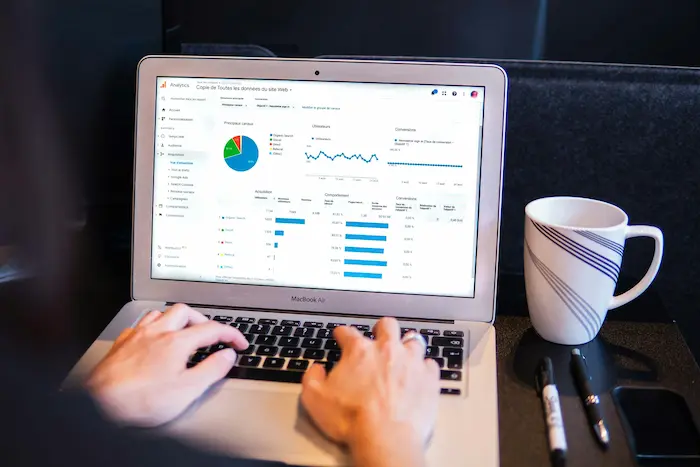 Personne analysant les données d’un site web sur Google Analytics avec un tableau de bord affichant les KPI : sources de trafic, comportement des utilisateurs et conversions.